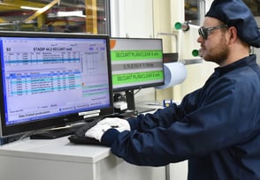 An employee works in the clean room with the A+W Production Terminals displayed on the monitors in front of him.