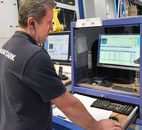 An employee stands in front of a monitor and the A+W Production Terminal is displayed on it.