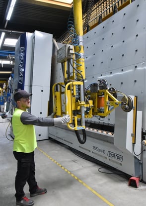 An employee stands in front of the vertical Systron grinding machine and machines rectangular lites.